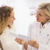 A female pharmacist explaining a prescription to a smiling female patient, at a pharmacy.