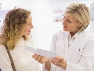 A female pharmacist explaining a prescription to a smiling female patient, at a pharmacy.