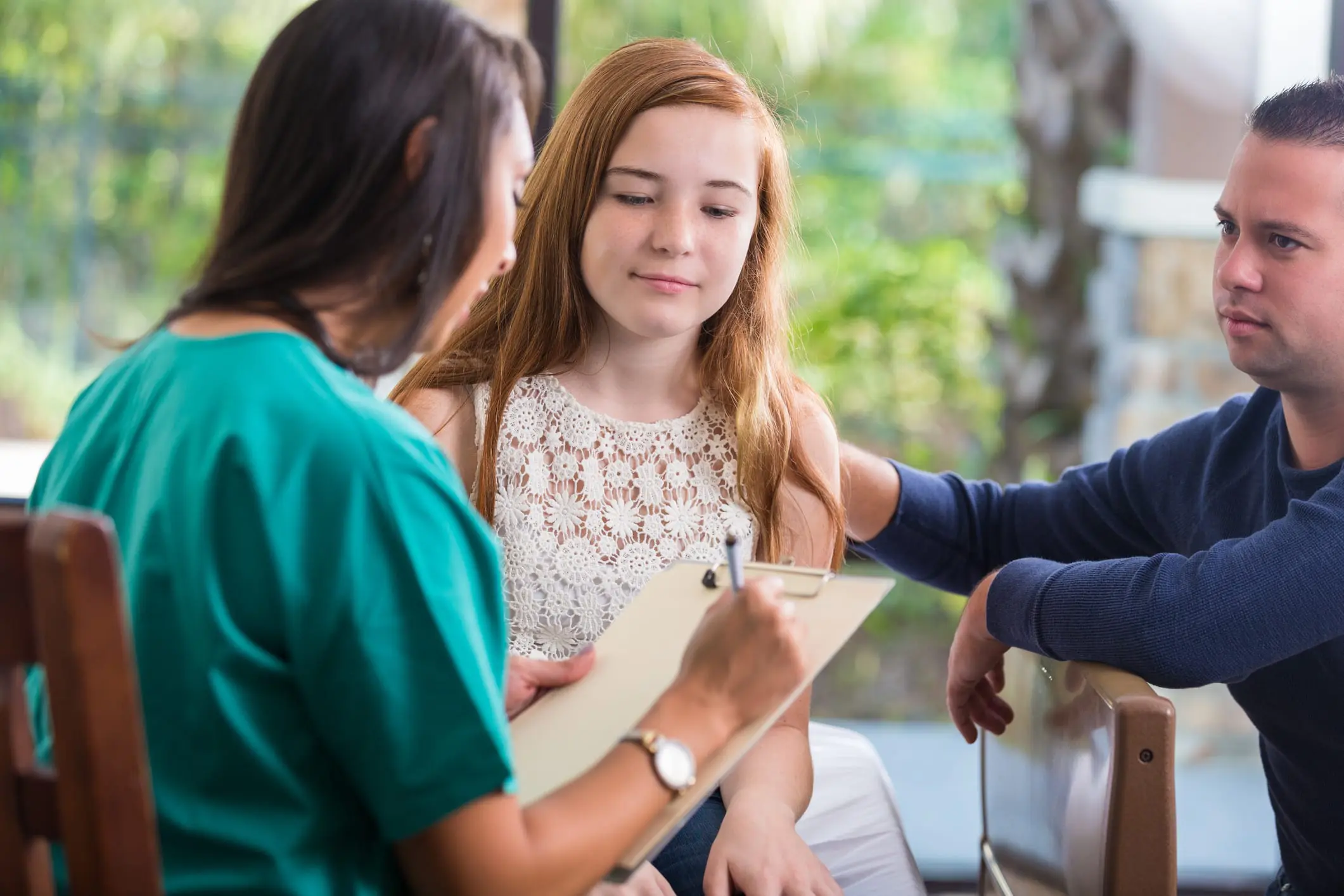 A female nurse writing on a clipboard helping treat a young female teen with her allergies.