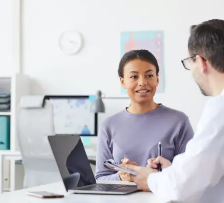 A female patient talking to a male doctor while sitting at a desk in the doctors office.