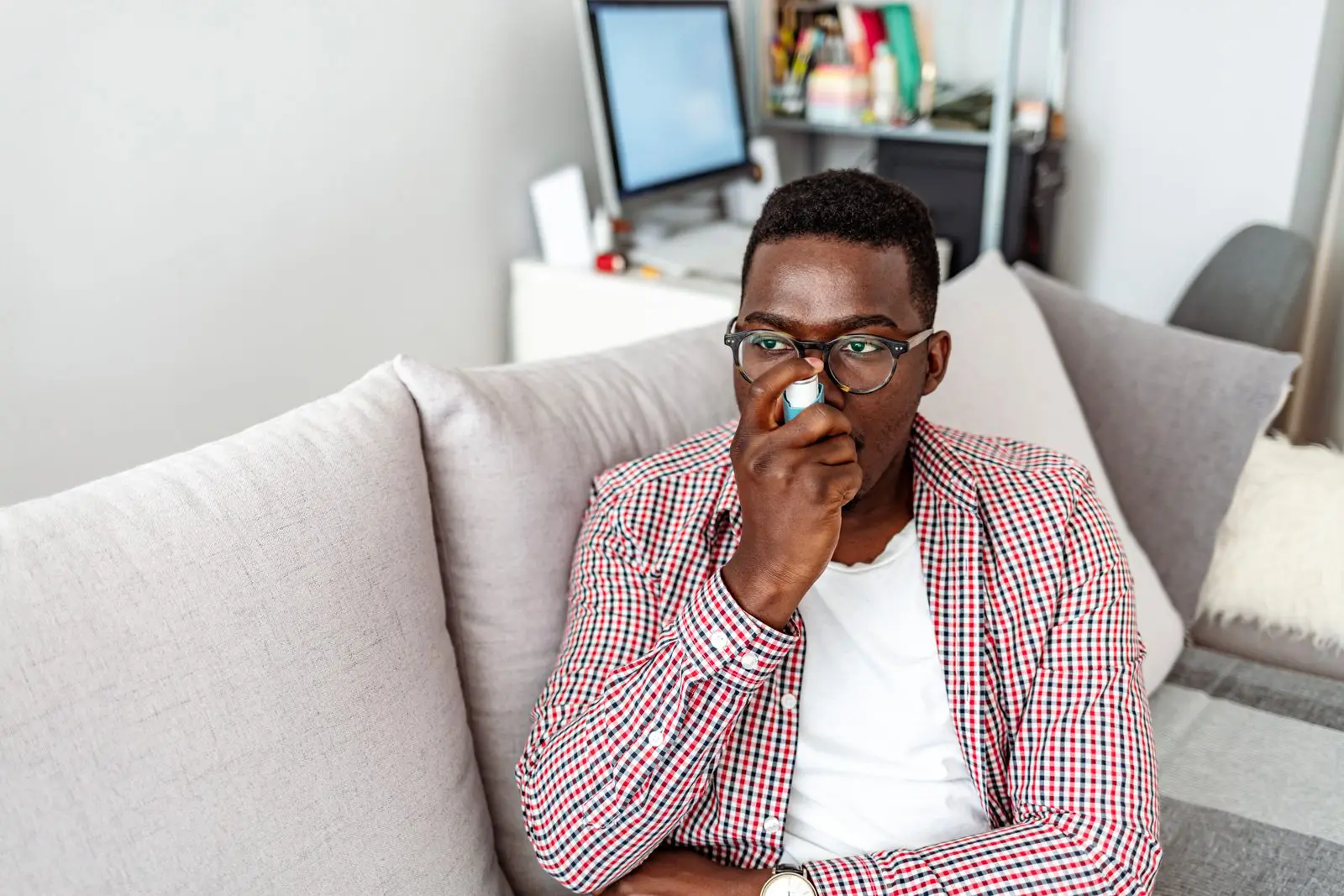 A young male using an inhaler while sitting on his couch at home.