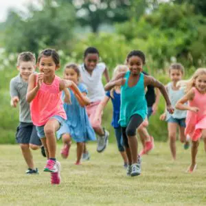 A group of young children running outside smiling while playing tag.