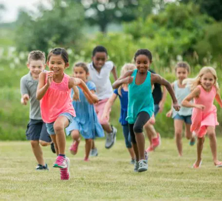 A group of young children running outside smiling while playing tag.