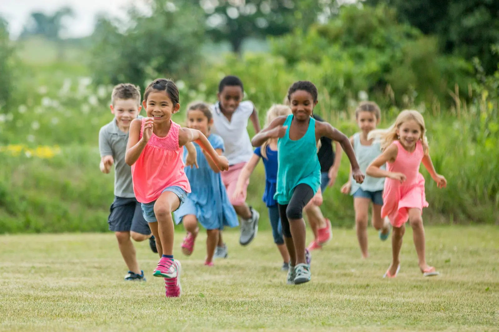 A group of young children running outside smiling while playing tag.
