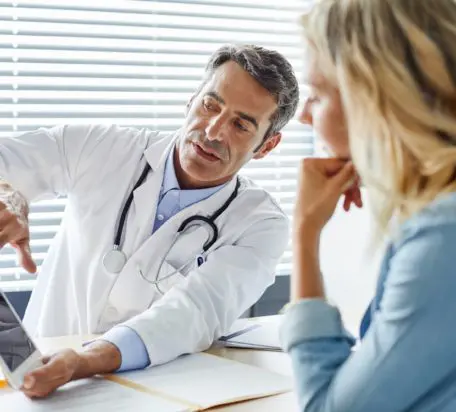 A male doctor showing a digital tablet to a female patient while both sitting in the doctor's office.