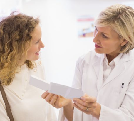 A female pharmacist explaining a prescription to a smiling female patient, at a pharmacy.