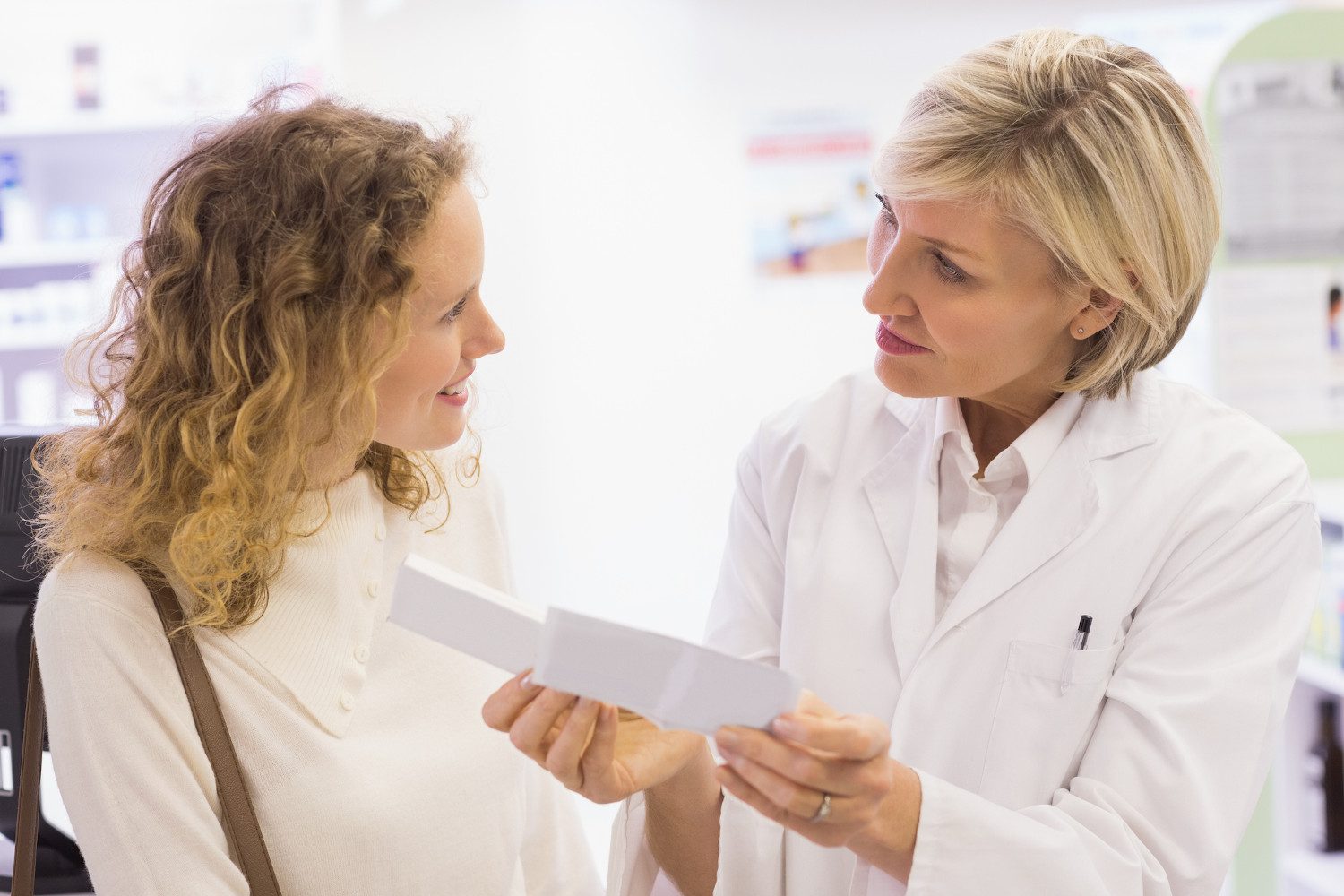 A female pharmacist explaining a prescription to a smiling female patient, at a pharmacy.